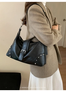 Close-up of black leather shoulder bag featuring silver rivets and wide buckle detail