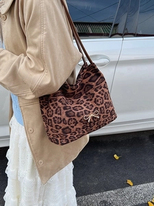 Leopard print tote bag with gold bow pendant worn with a stylish winter camel coat