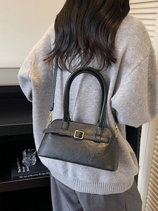 Minimalist black pebbled leather handbag with gold buckle shown in a lifestyle setting