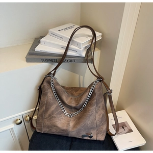 Detail of vintage brown tote bag featuring silver chain and heart charm in home setting