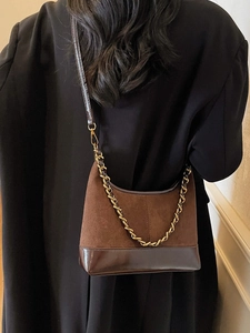 Brown suede dumpling bag with leather trim and gold chain strap worn as a shoulder bag