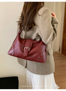 Detail of dark red retro tote bag with wide buckled strap and metallic silver rivets