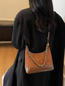 Brown suede hobo bag with gold chain strap worn over a black blazer for a retro style