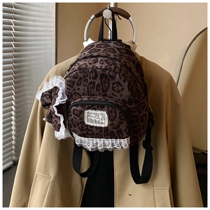 Detail of leopard print mini backpack featuring white lace edges and a small bow charm