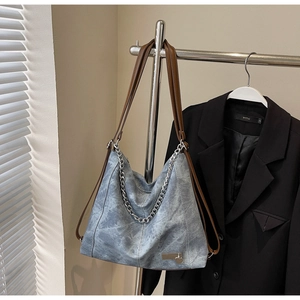 Detail of blue denim tote bag with brown leather straps and silver heart chain charm