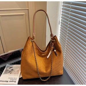 Detail of brown suede tote bag featuring metallic chain strap and beaded tassel charm