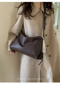 Detail of a large dark brown pebbled leather tote bag worn with an elegant wool coat