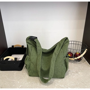 Detailed close-up of green corduroy tote bag texture with adjustable strap and side pocket