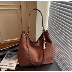 Detail of dark brown suede tote bag with golden twist lock and beaded charm accessory
