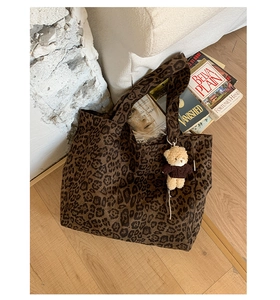 Leopard print canvas tote bag with a cute plush bear charm on a warm wooden floor