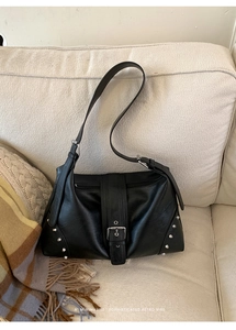 Detail of black faux leather tote with silver rivets and buckle on a soft white sofa