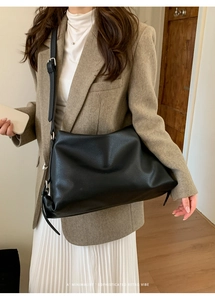 Side view of black pebble leather tote bag worn by a model in a minimalist setting
