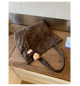 Detail of leopard print canvas tote bag with a cute plush bear charm on a wooden table