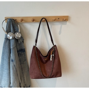 Close-up of retro brown suede tote bag featuring metallic chain and colorful bead charm