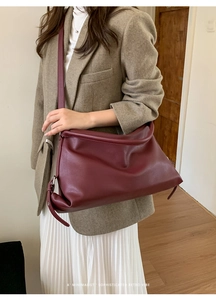 Detail of burgundy half-moon shoulder bag with soft lychee texture on grey blazer