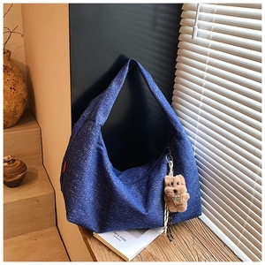 Detail view of a navy blue denim hobo bag featuring a cute brown plush bear charm