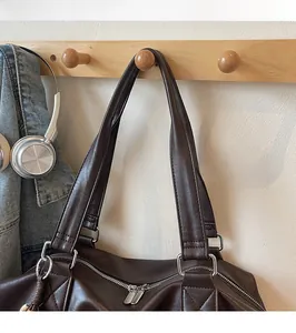 Détail du sac en cuir marron avec anneaux argentés et franges sur un support en bois