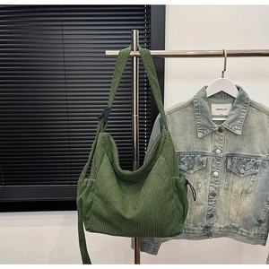 Detailed texture of green corduroy hobo bag with side pockets hanging on a metal rack