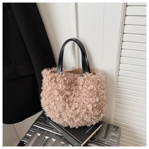 Plush beige faux shearling bucket bag with black leather handles on a suitcase