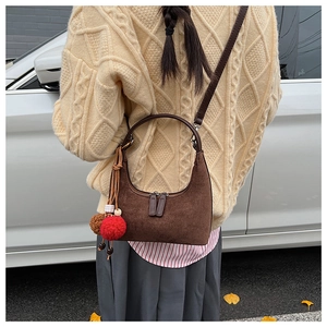 Détail du sac demi-lune en daim marron avec double fermeture éclair et pompon élégant