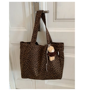 Detail of leopard print canvas tote bag with brown plush bear charm and side brand label