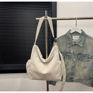 Close-up of cream corduroy tote bag texture and side pocket on a metal display stand
