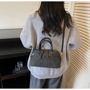 Close-up of a black quilted shell bag with gold hardware worn by a model in a minimalist room