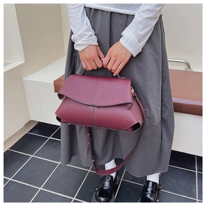 Detail of burgundy leather shoulder bag featuring white contrast stitching and tiered flap