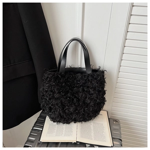 Detail view of black faux shearling tote bag with leather handles on an open book