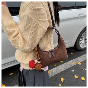 Détail d'un sac hobo en daim marron foncé avec pompons dans un décor d'automne extérieur