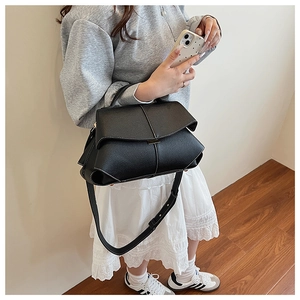 Detail view of black leather shoulder bag with white contrast stitching and gold buckle