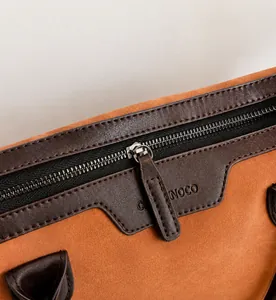 Detailed close-up of smooth metal zipper and brand embossing on brown tote bag