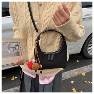 Détail d'un sac sous le bras noir en forme de croissant avec pompons décoratifs