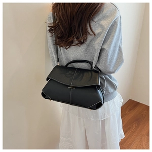 Detail view of black leather shoulder bag with contrast white stitching and minimalist flap
