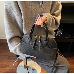 Detail view of black quilted shell bag featuring gold zippers and cylindrical top handles