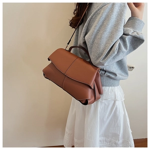 Detailed side view of a brown leather flap shoulder bag worn by a model in a warm setting