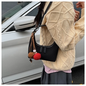 Détail du sac hobo en nylon noir avec breloque pompon rouge et marron sur la bandoulière