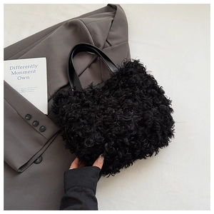 Dettaglio di una borsa a secchiello in peluche nero con manici in pelle liscia