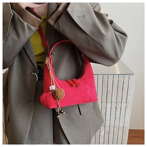 Détail du sac demi-lune rouge en daim avec pompons décoratifs porté par un mannequin en costume