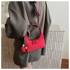 Gros plan sur le sac demi-lune en daim rouge avec pompon et breloque en perles de bois