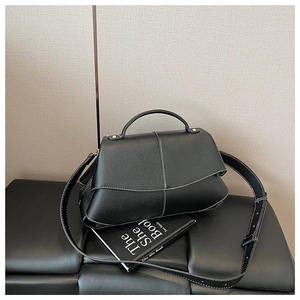 Detail of black pebbled leather handbag featuring white contrast stitching and curved handle