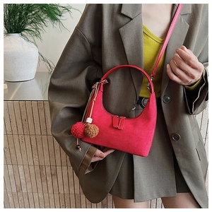 Détail du sac demi-lune en daim rouge avec pompon bicolore et bandoulière amovible