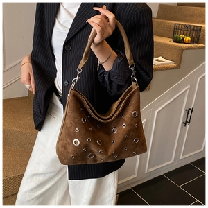 Détail d'un sac à bandoulière en daim marron foncé avec œillets argentés et rivets