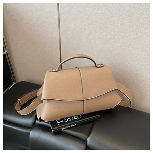 Detail view of light brown pebble leather handbag with top handle on a black leather bench