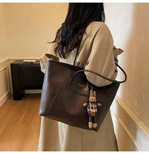 Detail of dark brown tote bag with leather texture and cute rabbit charm on a model