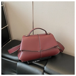 Detail of burgundy lychee grain leather shoulder bag with trapezoid structure and metal trim