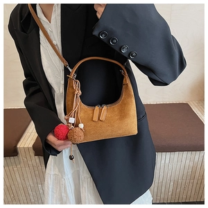 Détail du sac hobo en daim marron avec pompon décoratif et bandoulière élégante en gros plan