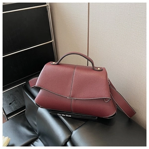 Close-up of burgundy lychee grain leather handbag with detailed white stitching and gold hardware