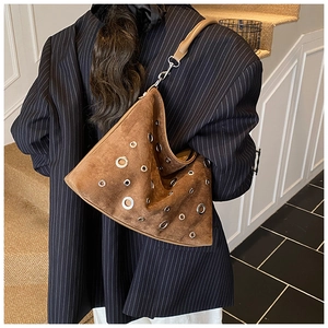 Sac à bandoulière en daim marron avec œillets argentés porté par un mannequin en costume