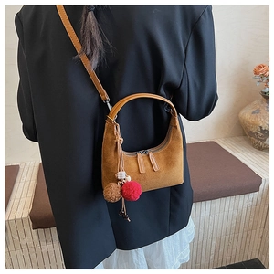 Détail du sac croissant en daim caramel avec pompons en peluche et finitions argentées